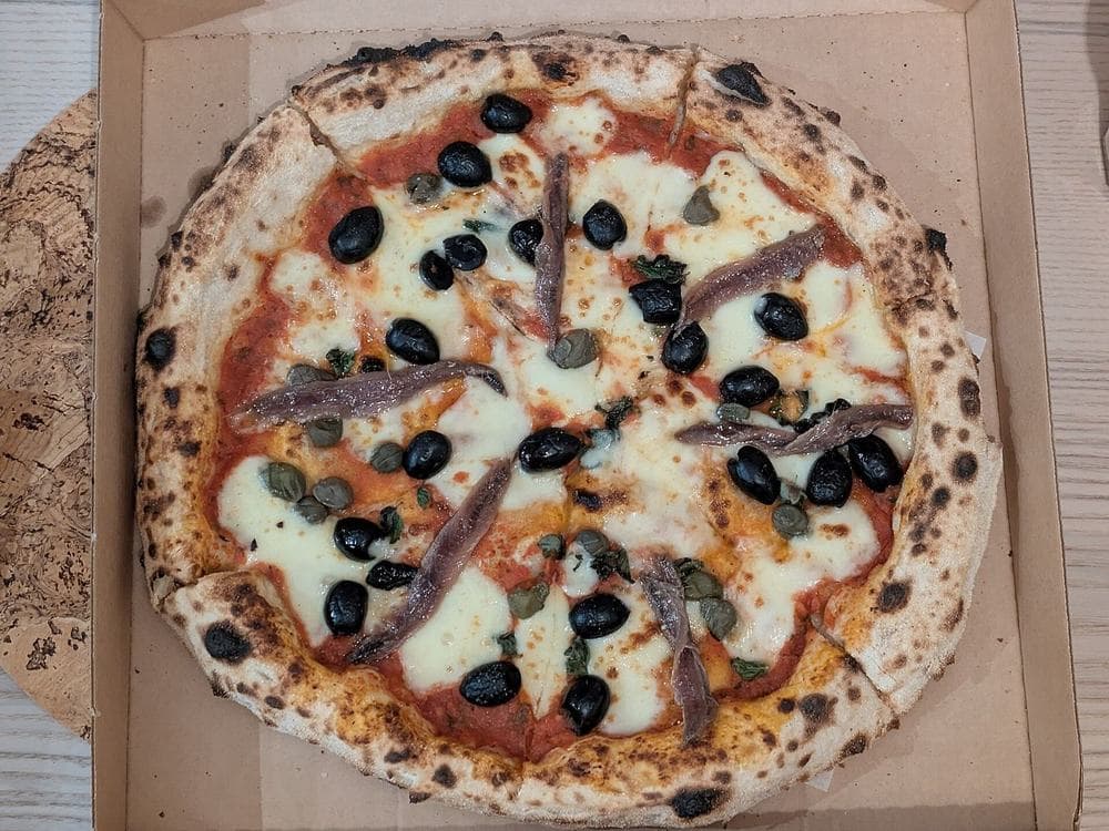 Pizza con alici, olive nere, capperi e origano